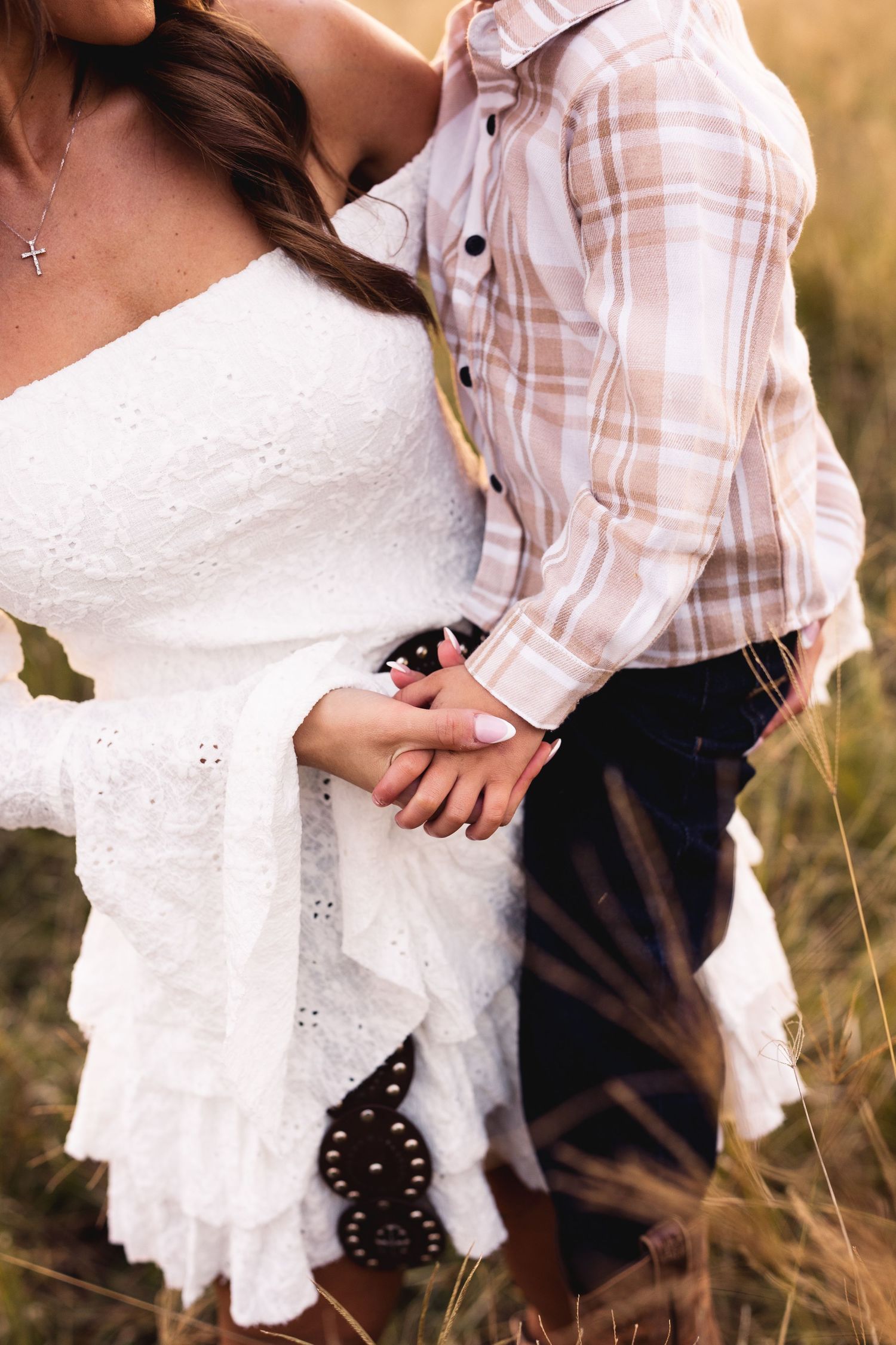 Close-up of mother and young boy holding hands in sunny field, woman in white lace dress.