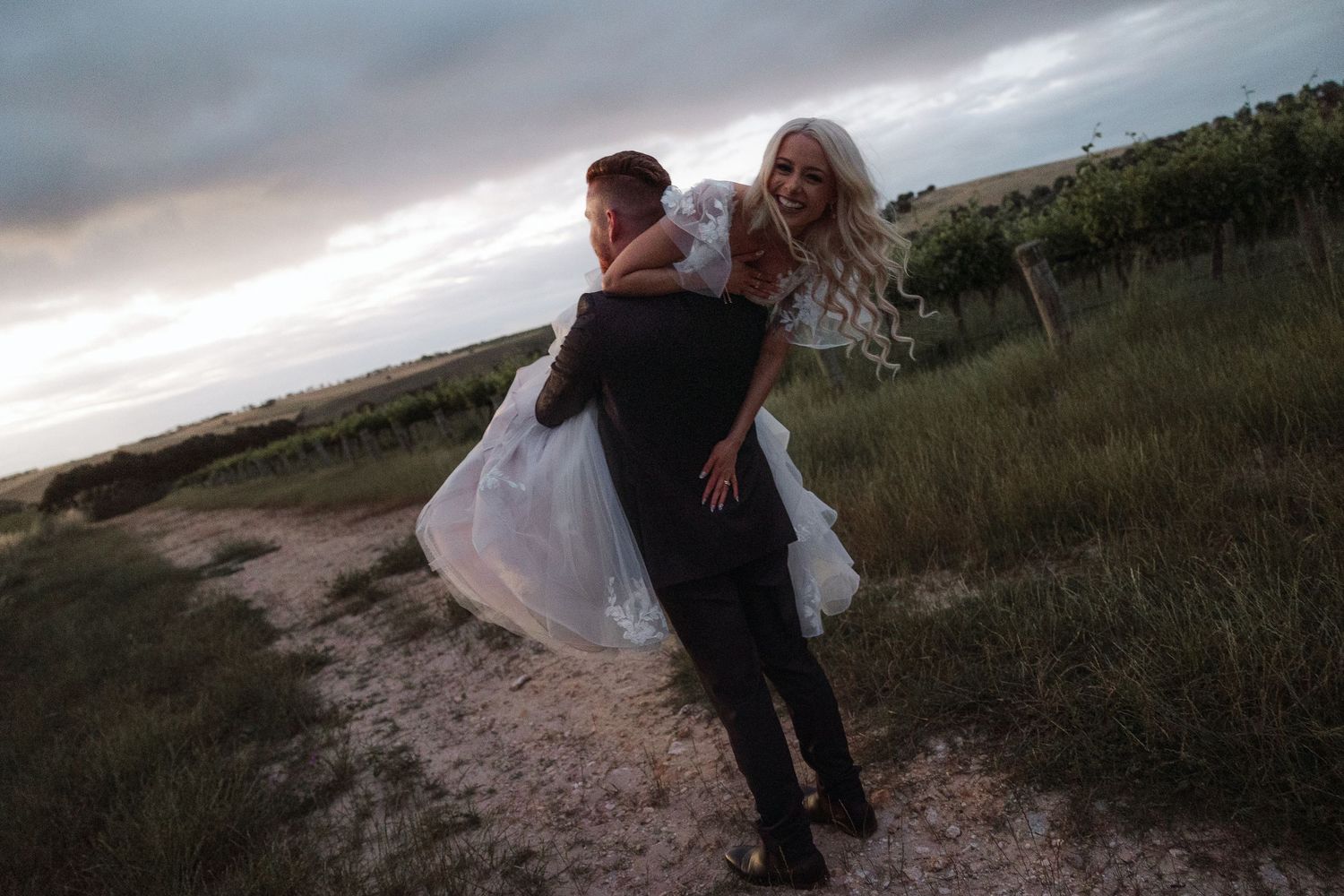 A couple in wedding attire embraces on a vineyard. Gomersal Wines