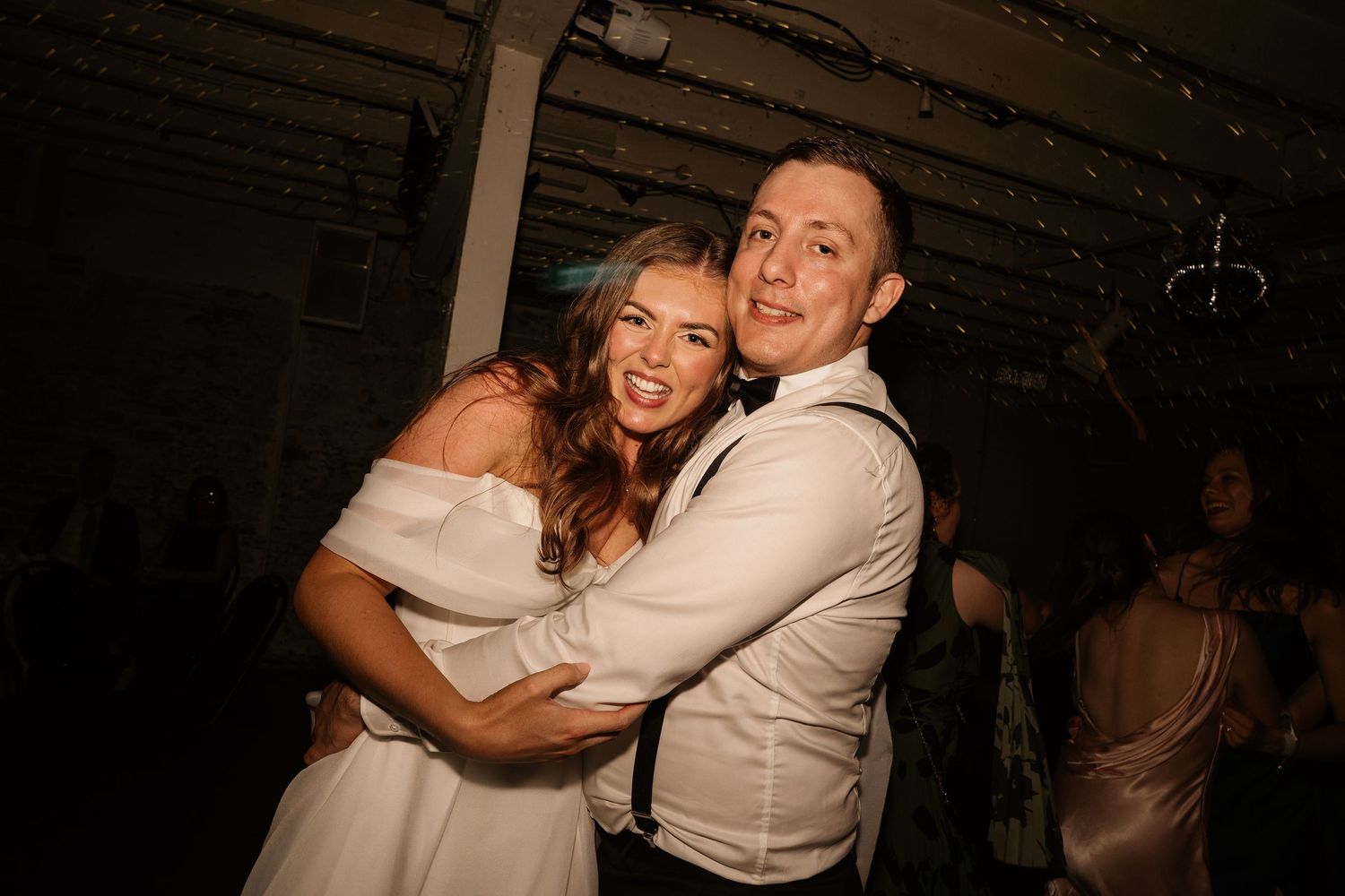 A couple shares a joyful dance moment together at a dimly lit reception venue.