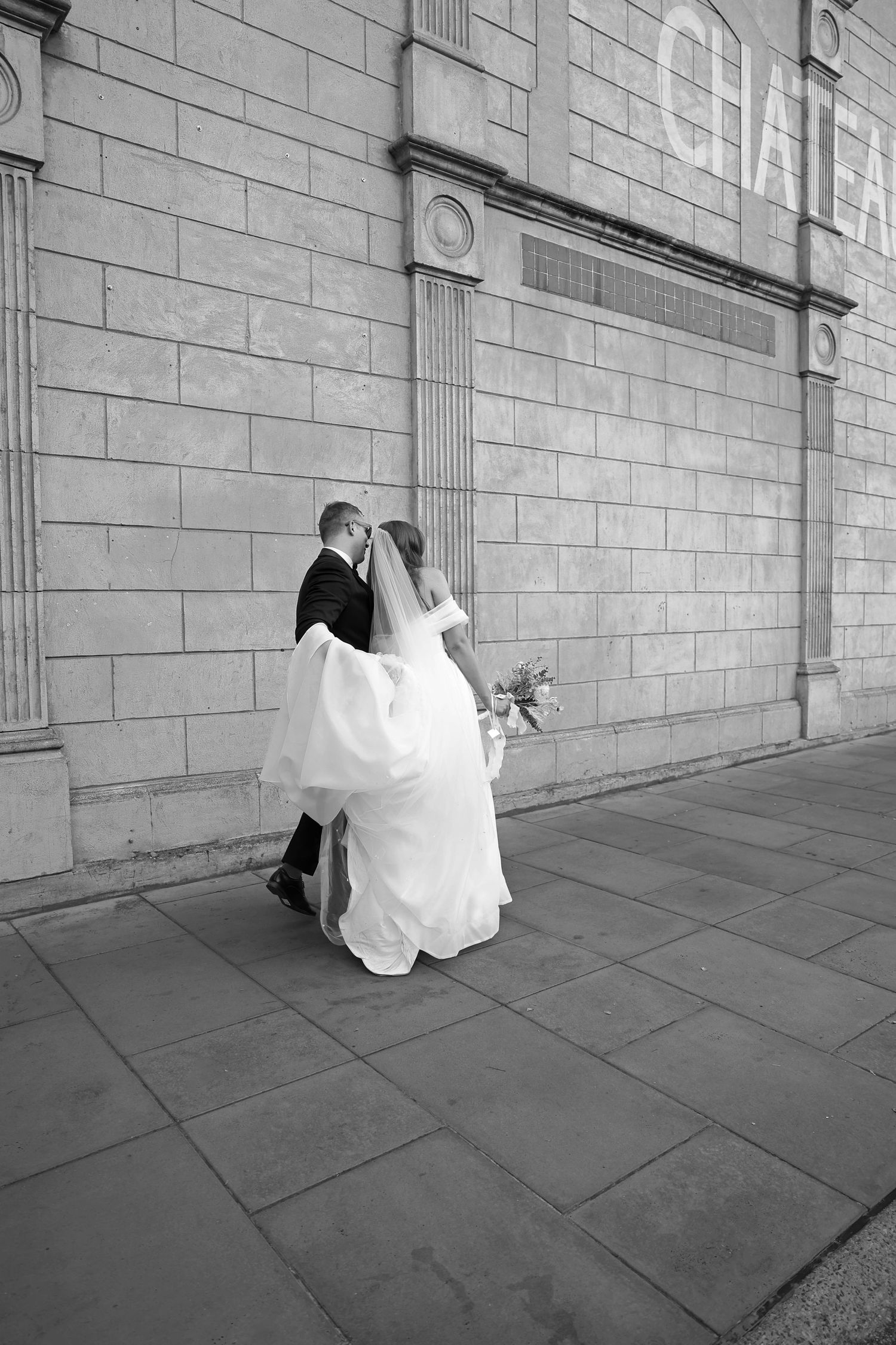 Wedding couple dances and twirls against a grand stone building exterior.
