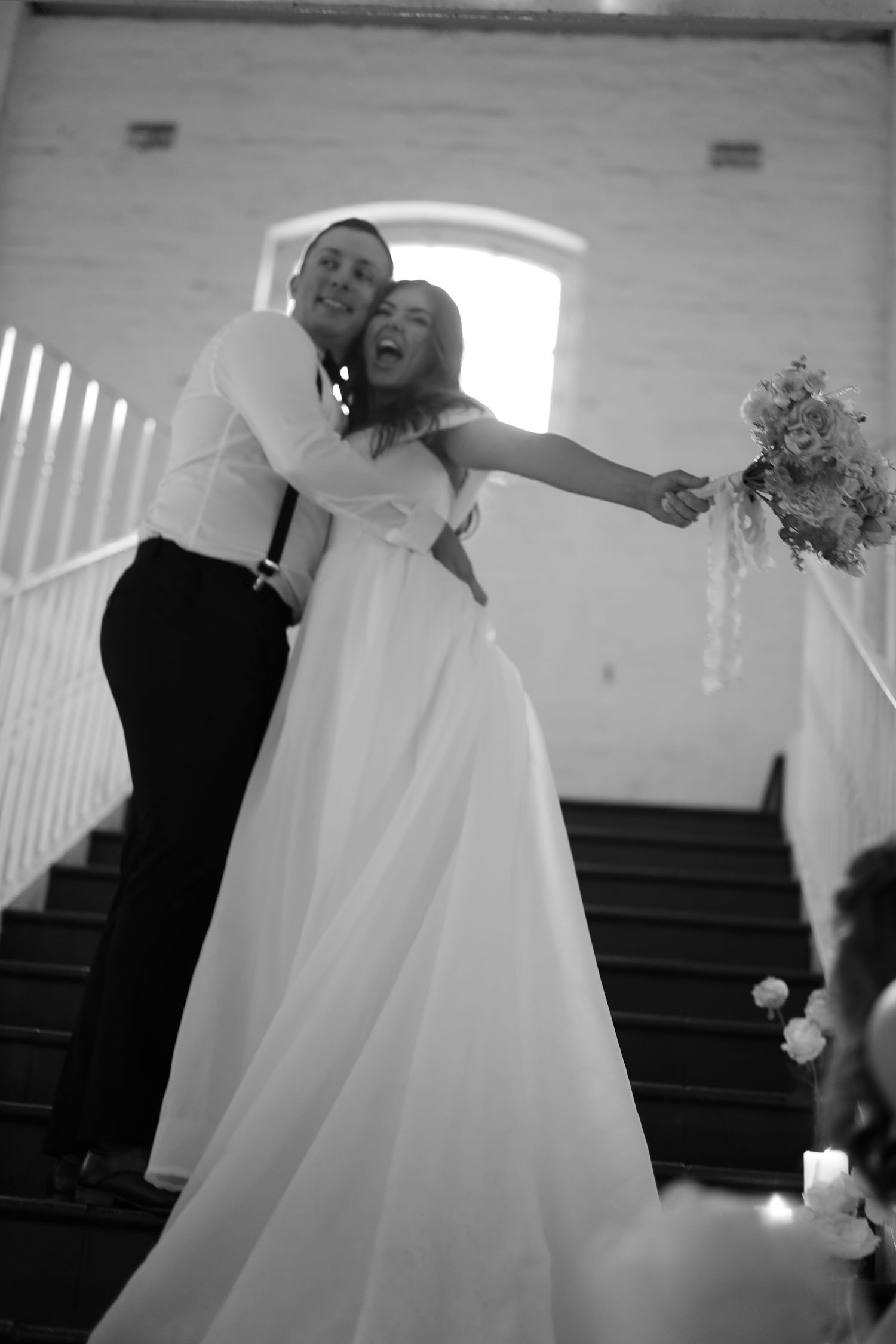 A joyful wedding moment captured in black and white as a couple celebrates on stairs.