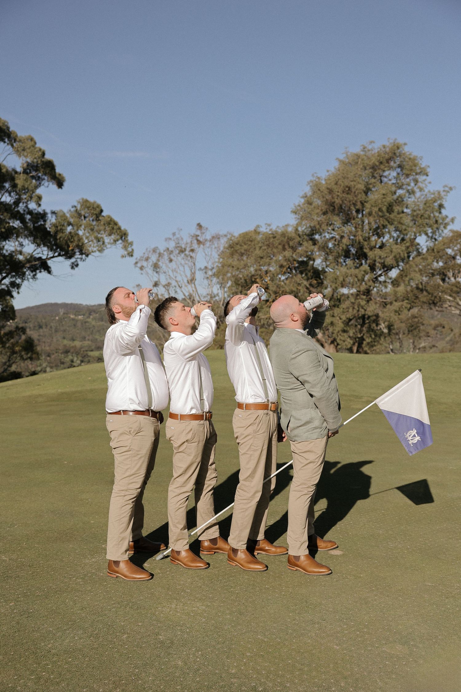 Groomsmen in matching khaki pants and white shirts strike a synchronized pose on a golf course green.