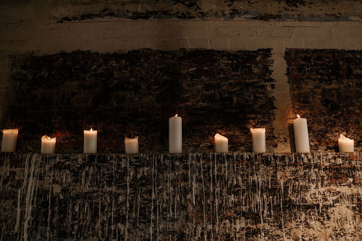 Row of white candles glowing against dark textured wall creating romantic ambiance.