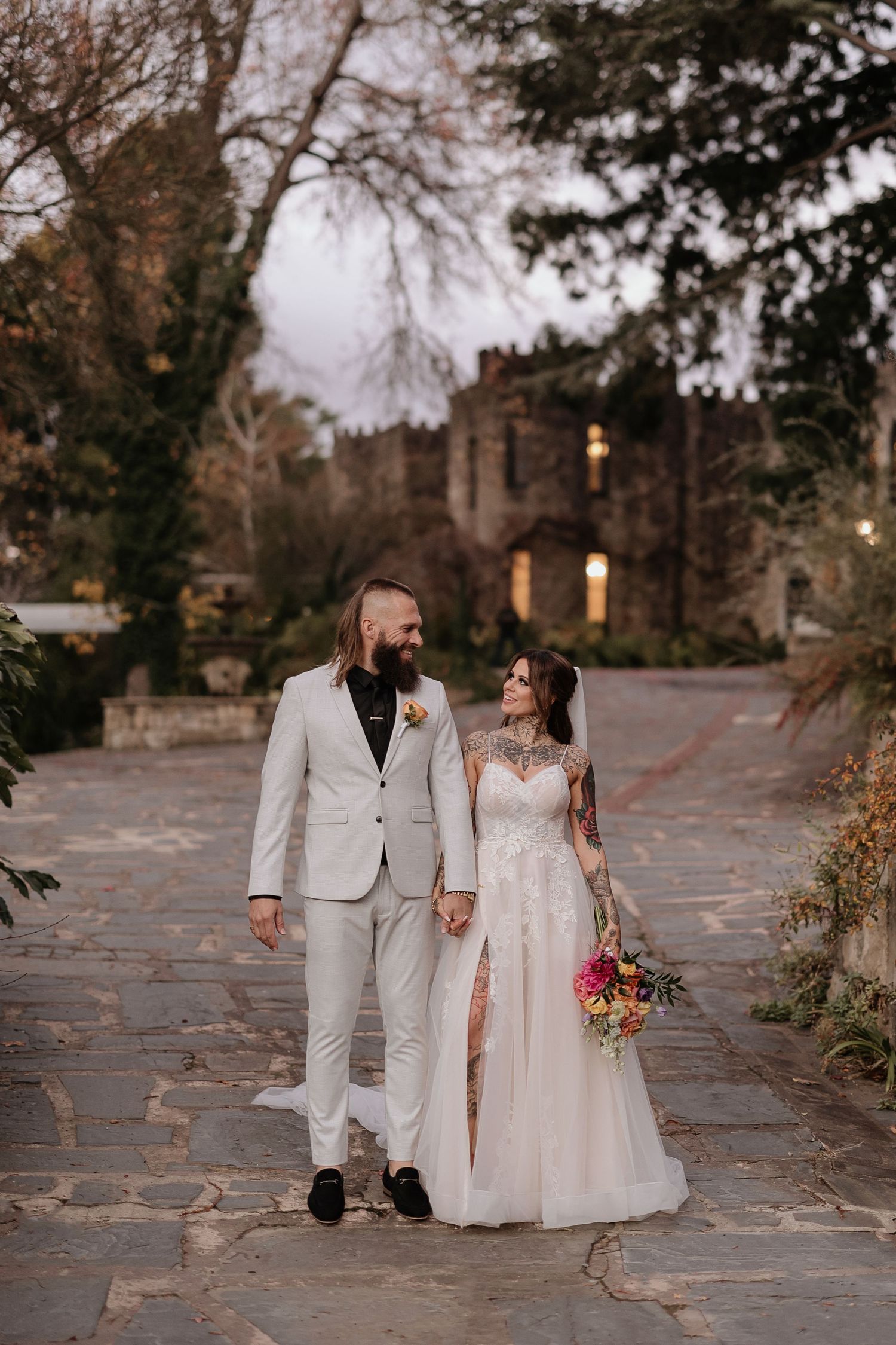 A couple walks together along a stone path during their autumn wedding at dusk.
