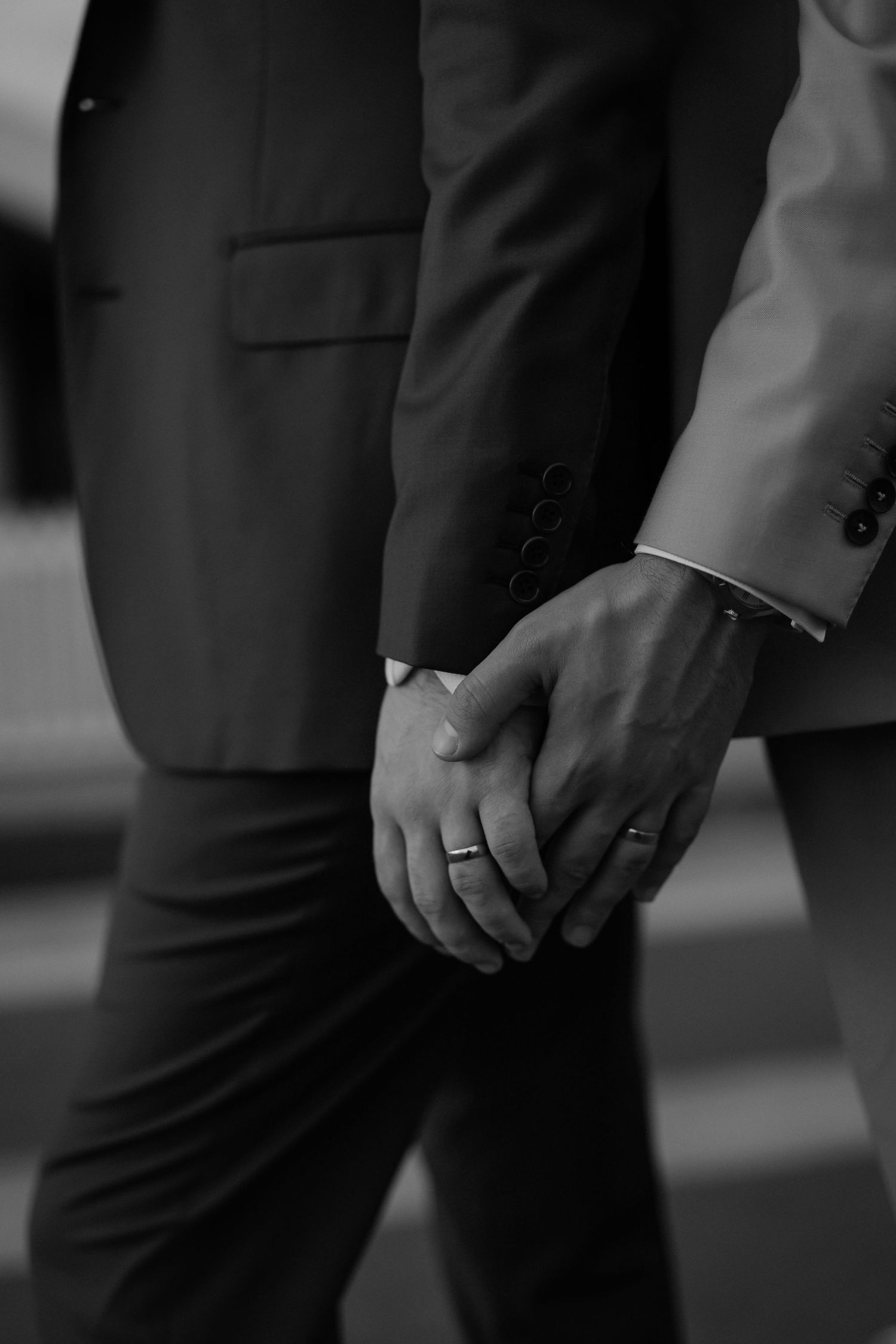 Close-up black and white detail of formal suits and hands during a wedding ceremony.