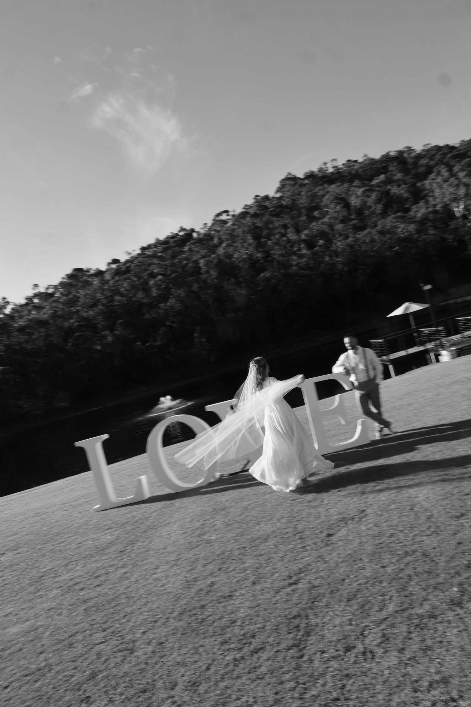 A black and white wedding photo with large LOVE letters and a flowing bridal gown against a mountain backdrop.