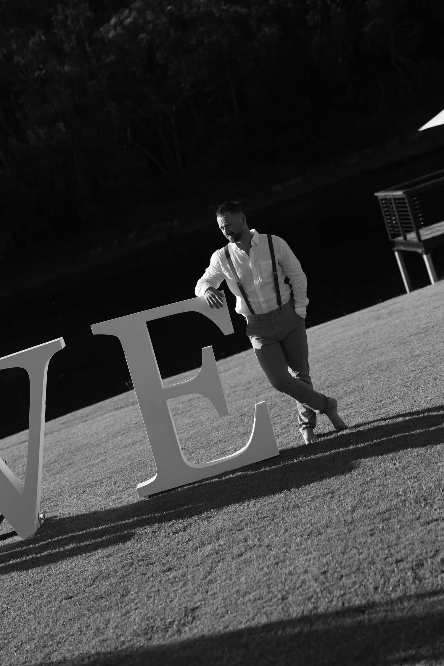 Black and white photo showing large decorative white letters being arranged on grass.