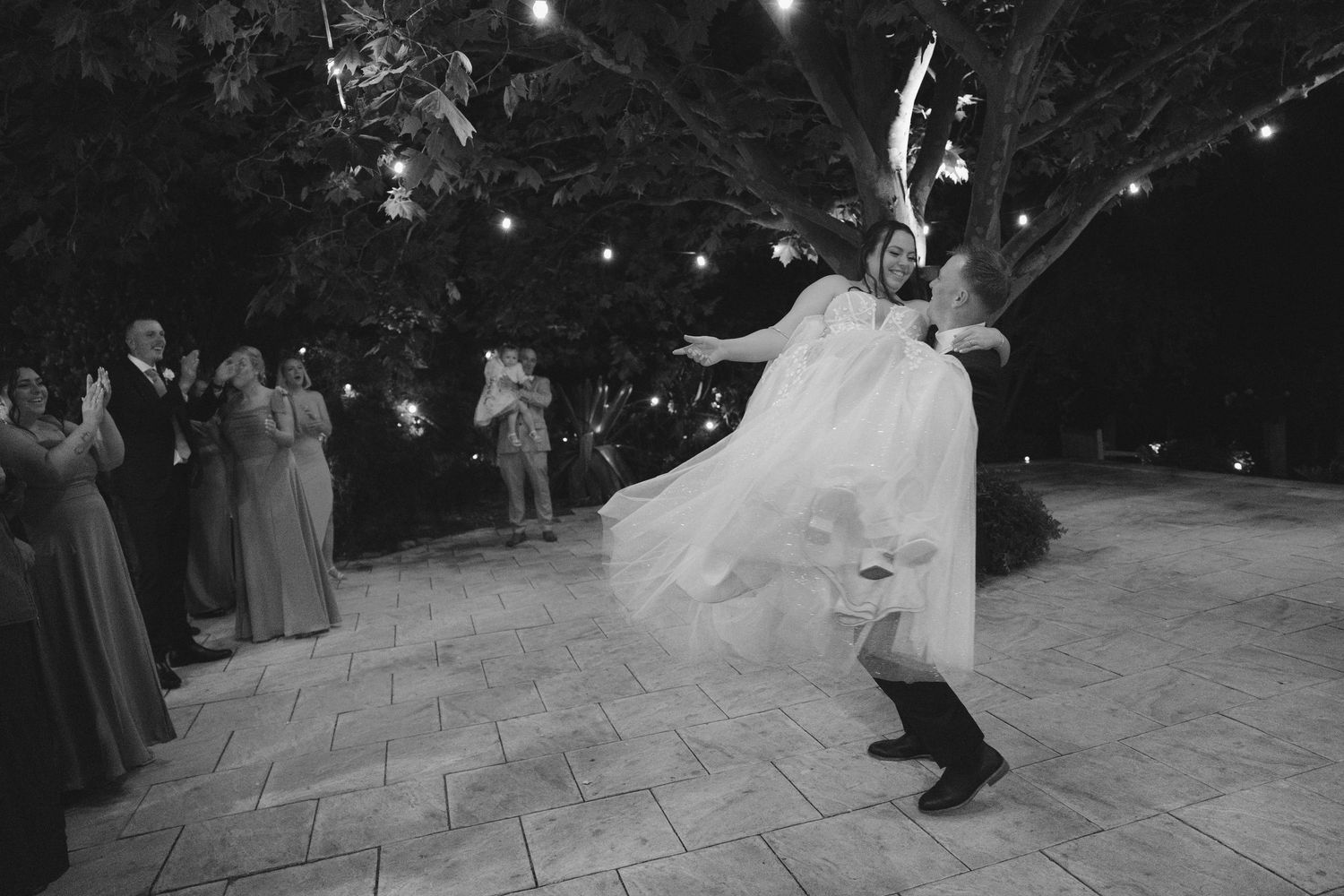 A couple shares their first dance on an illuminated outdoor dance floor at a nighttime wedding reception.