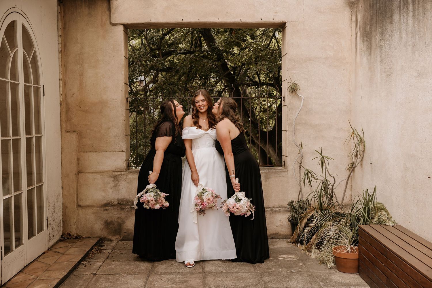 Wedding party members walk down an outdoor corridor with white stone walls and natural lighting.