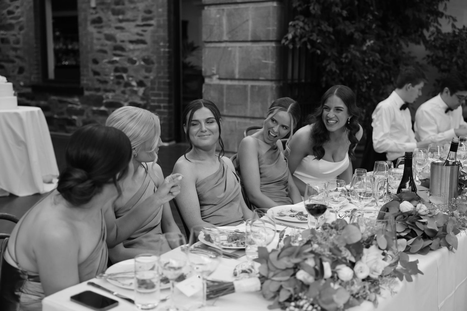 Wedding guests enjoy an elegant outdoor dinner reception at long tables decorated with floral centerpieces and glassware.