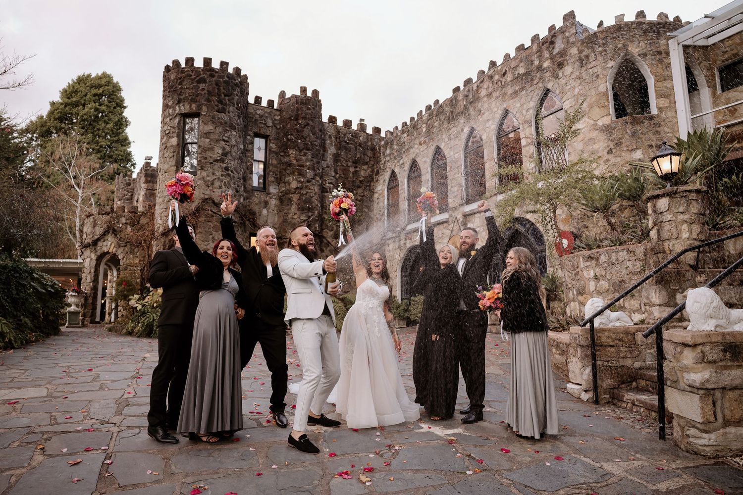 A wedding ceremony takes place in front of a historic stone castle wall with elegant decor and guests in formal attire.