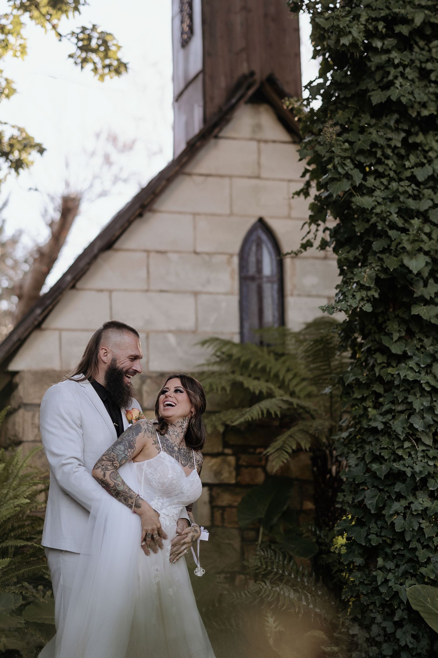 A romantic wedding moment captured outside a charming stone church with gothic windows and lush greenery.