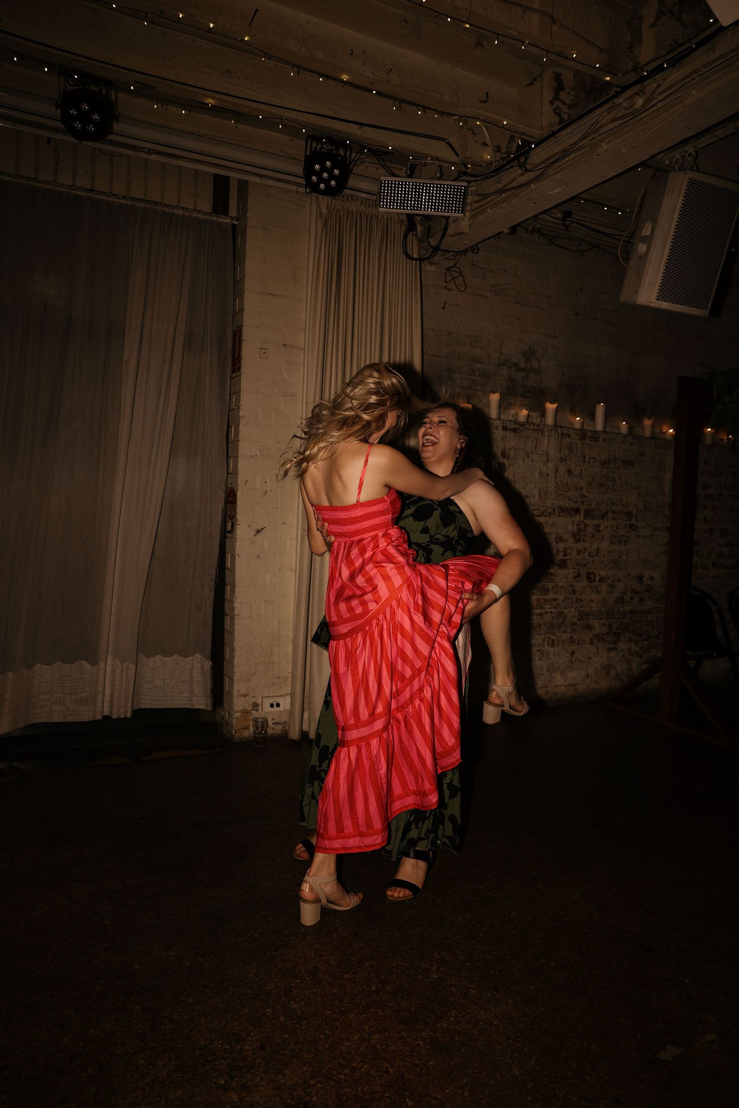 A dancer in a flowing red dress performs an expressive contemporary dance movement in a dimly lit studio space.