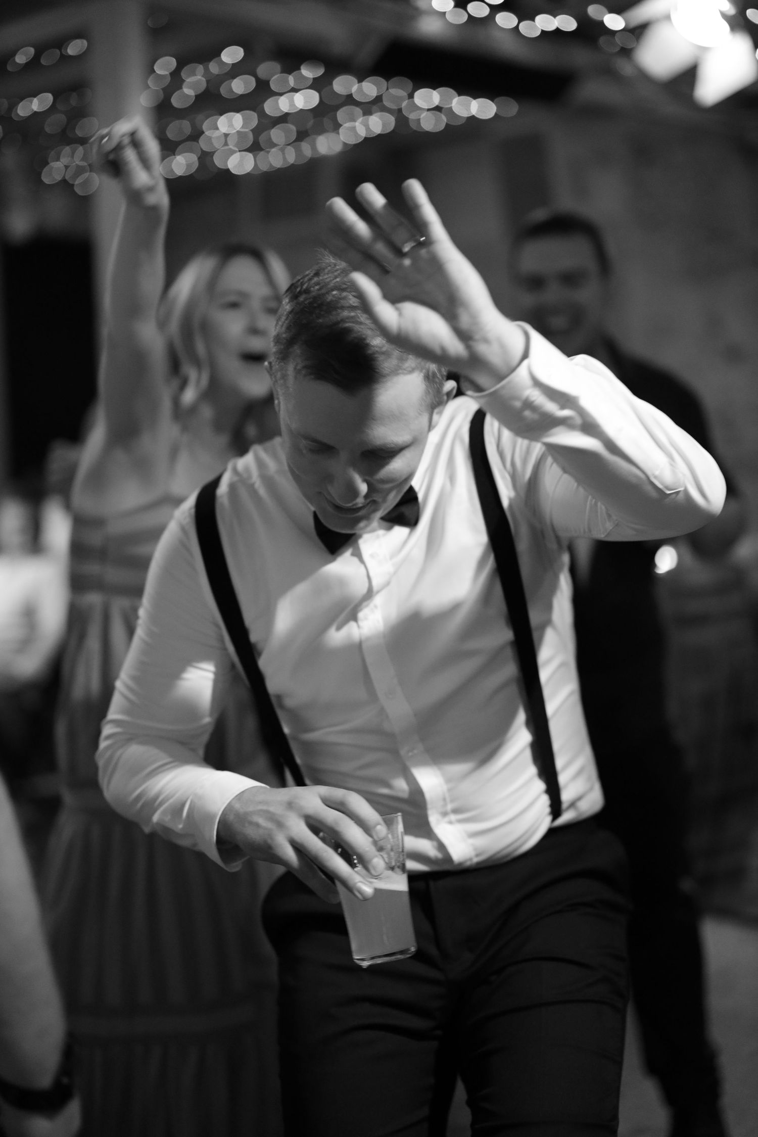 Black and white photo of people dancing at a party with someone in suspenders and white shirt enjoying themselves.