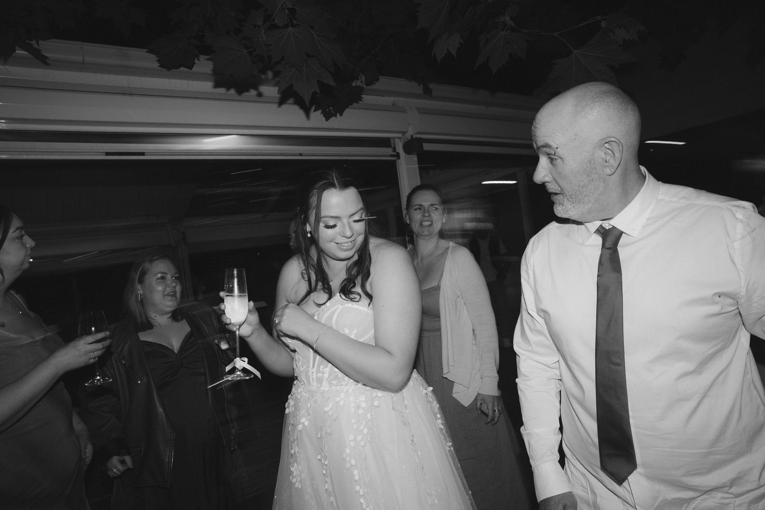 A black and white photo shows people dancing and celebrating at a lively wedding reception party.