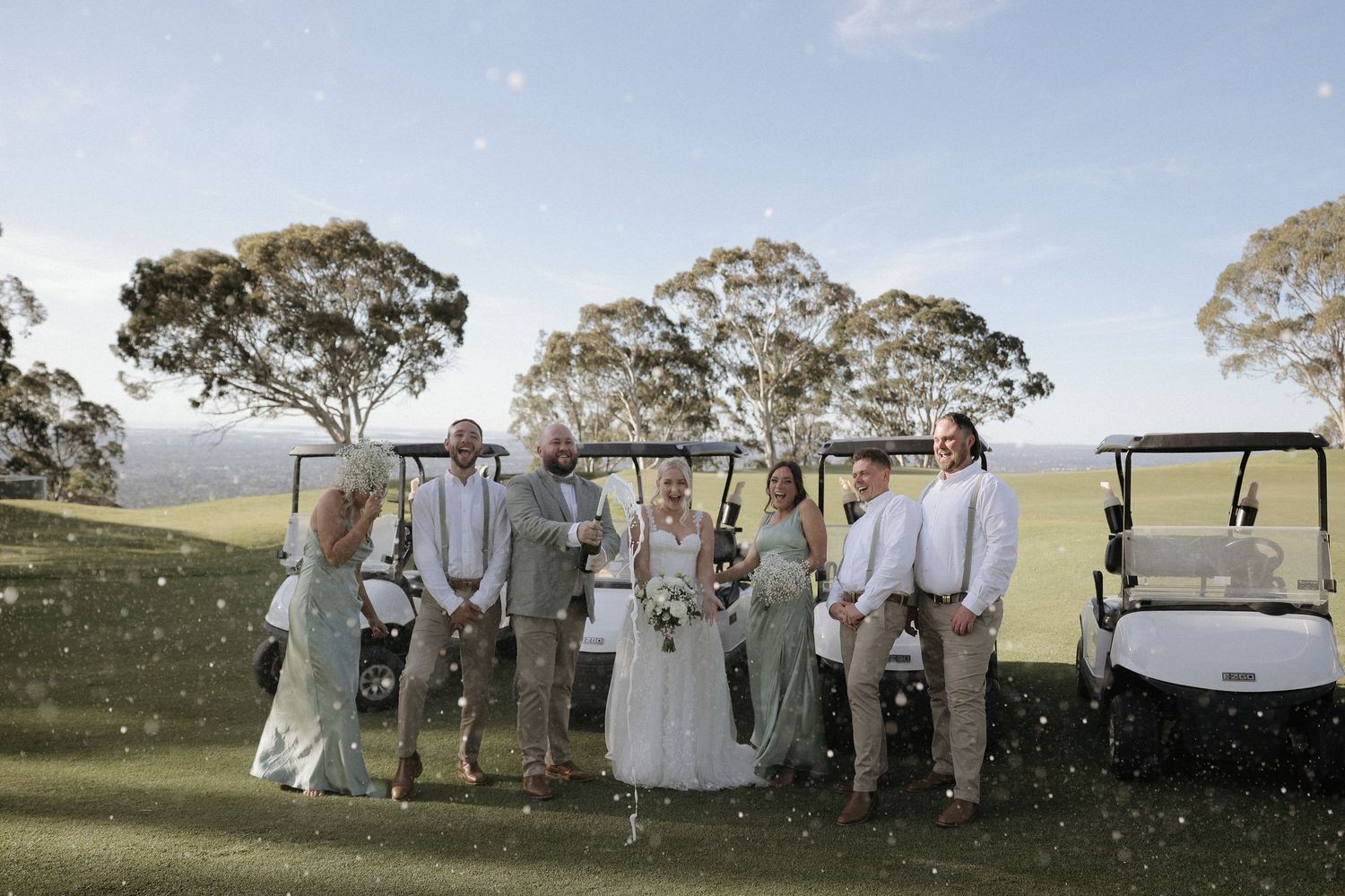 Wedding party walking through a scenic field at sunset with trees in the background.