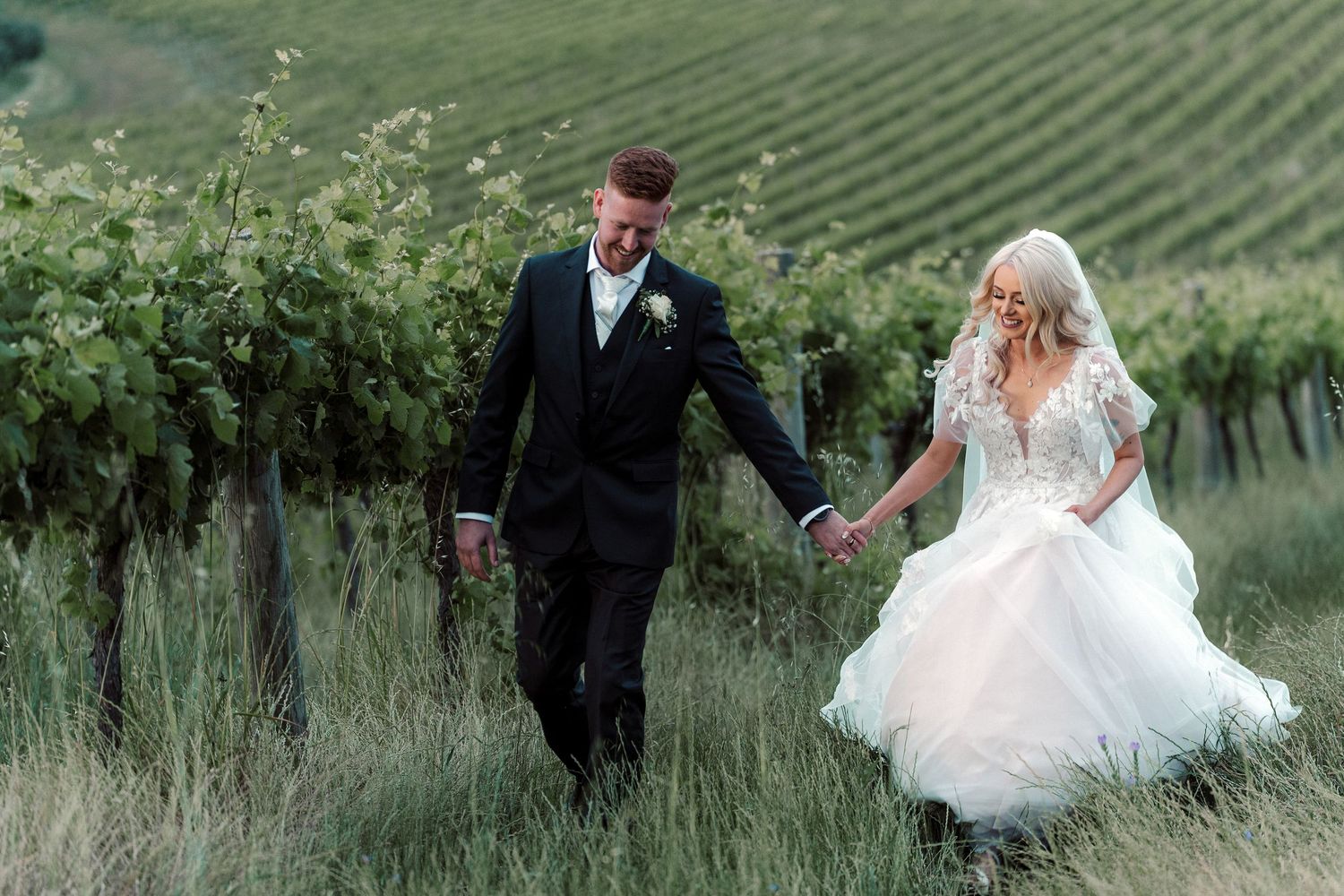 A couple celebrates their wedding day among scenic vineyard rows on a lush green hillside.