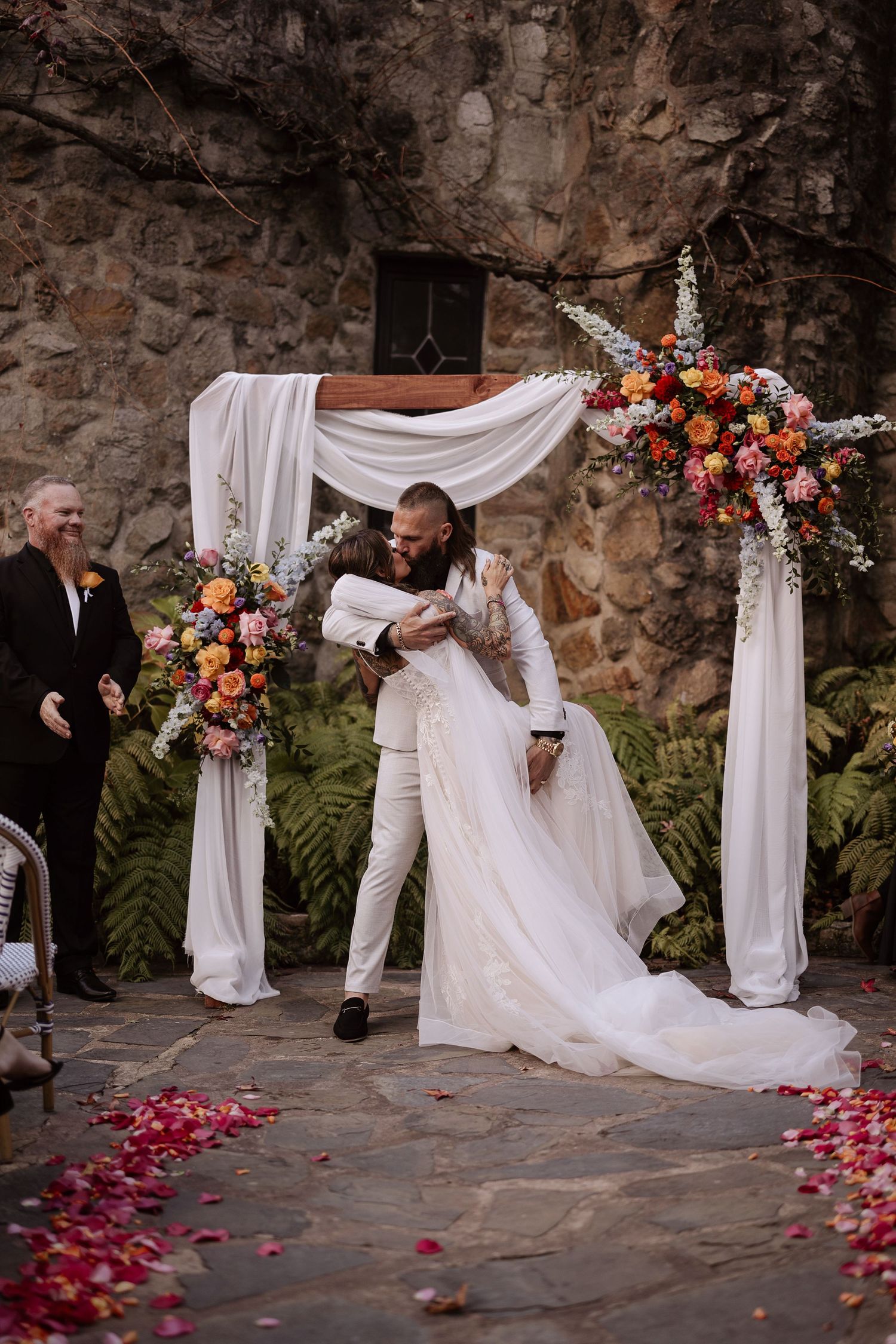 Sequence of wedding photos showing a bride falling during ceremony on stone patio with white draping and floral arch.