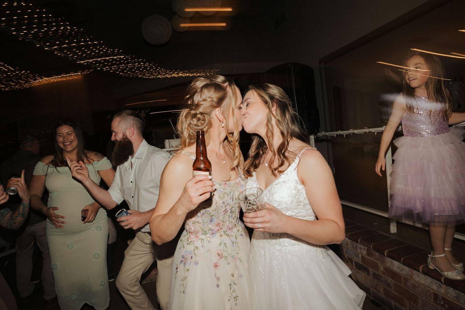 Wedding guests dancing and celebrating under string lights in an industrial-style venue.