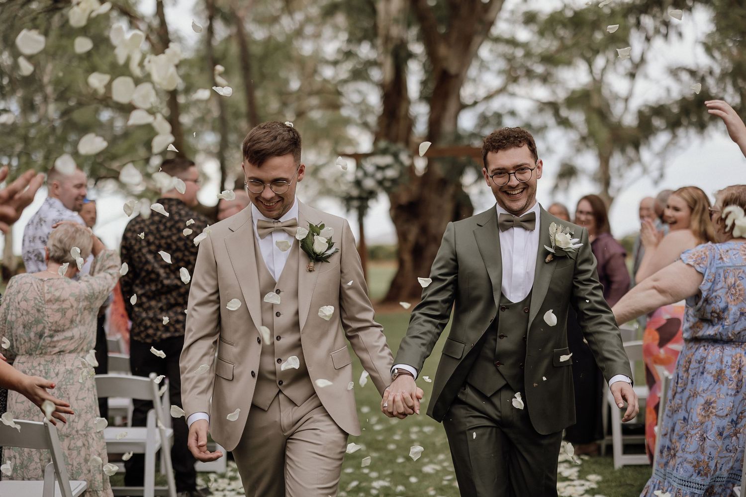 Wedding party members in tan and dark suits share joyful moments during an outdoor celebration.