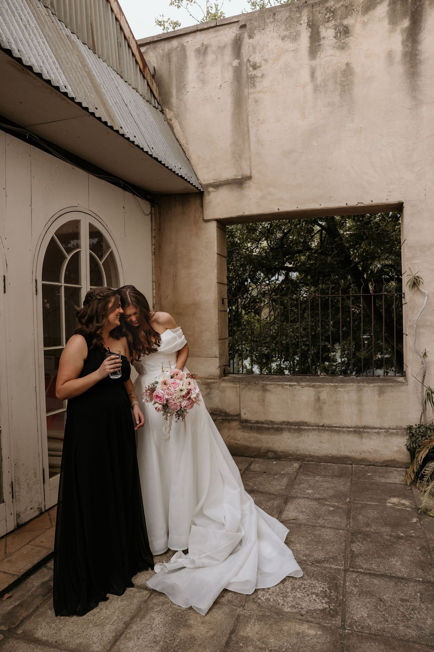 A person in a black dress kneels beside a white wedding gown on a concrete balcony.