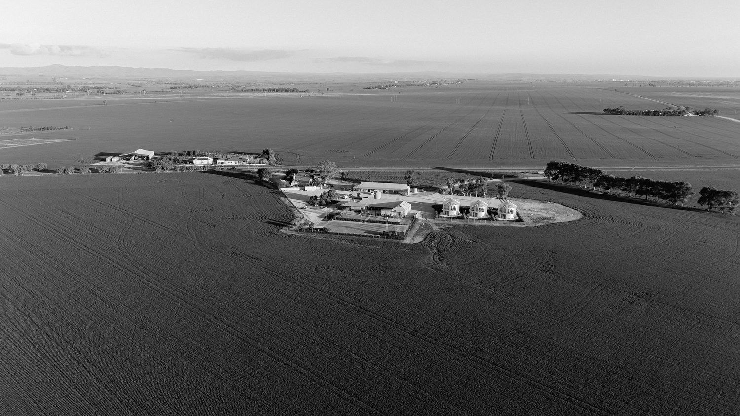A panoramic black and white aerial view shows a coastal landscape with scattered buildings and water features.