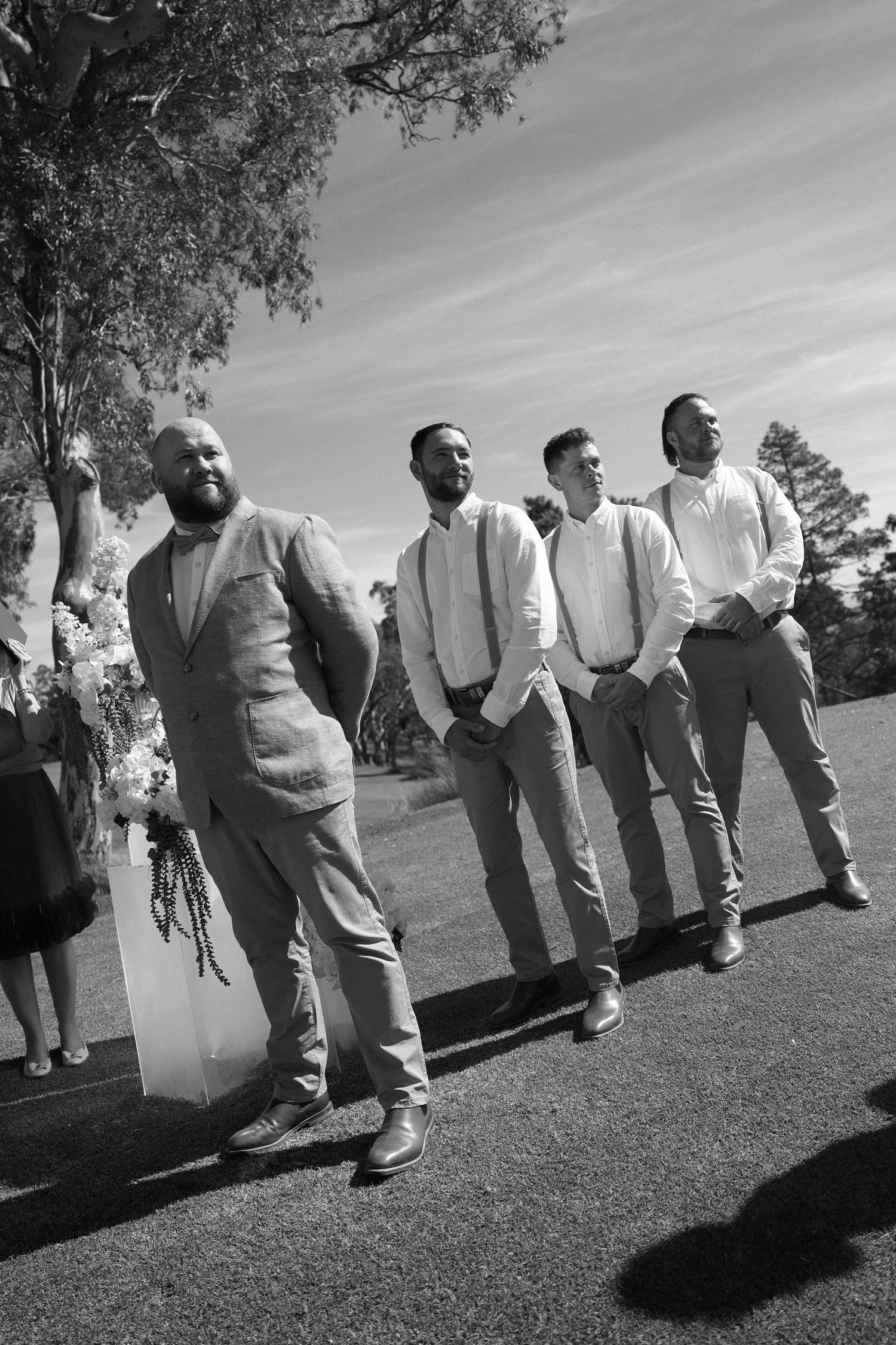 A black and white photo showing four people standing together outdoors in casual attire on a sunny day.