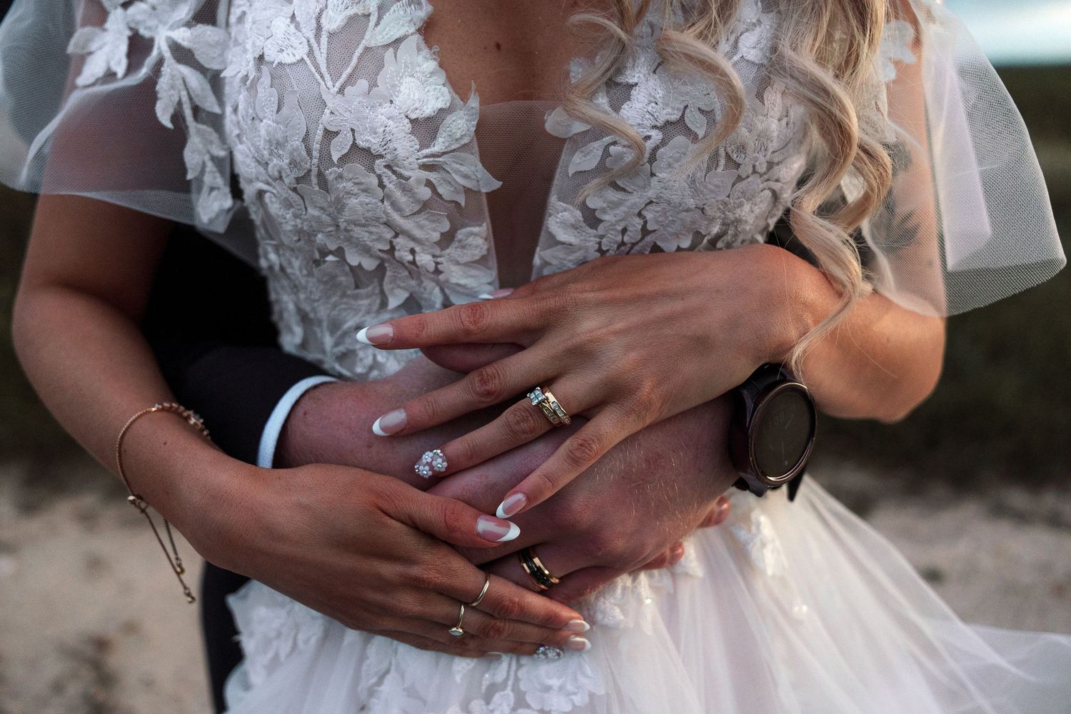 Close-up detail of hands with rings on intricate white lace wedding dress.