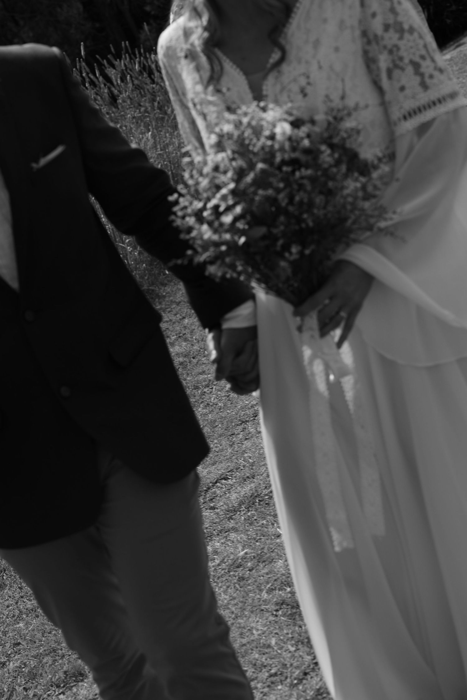 A wedding couple stands close together outdoors with white floral bouquets and formal attire visible in black and white.