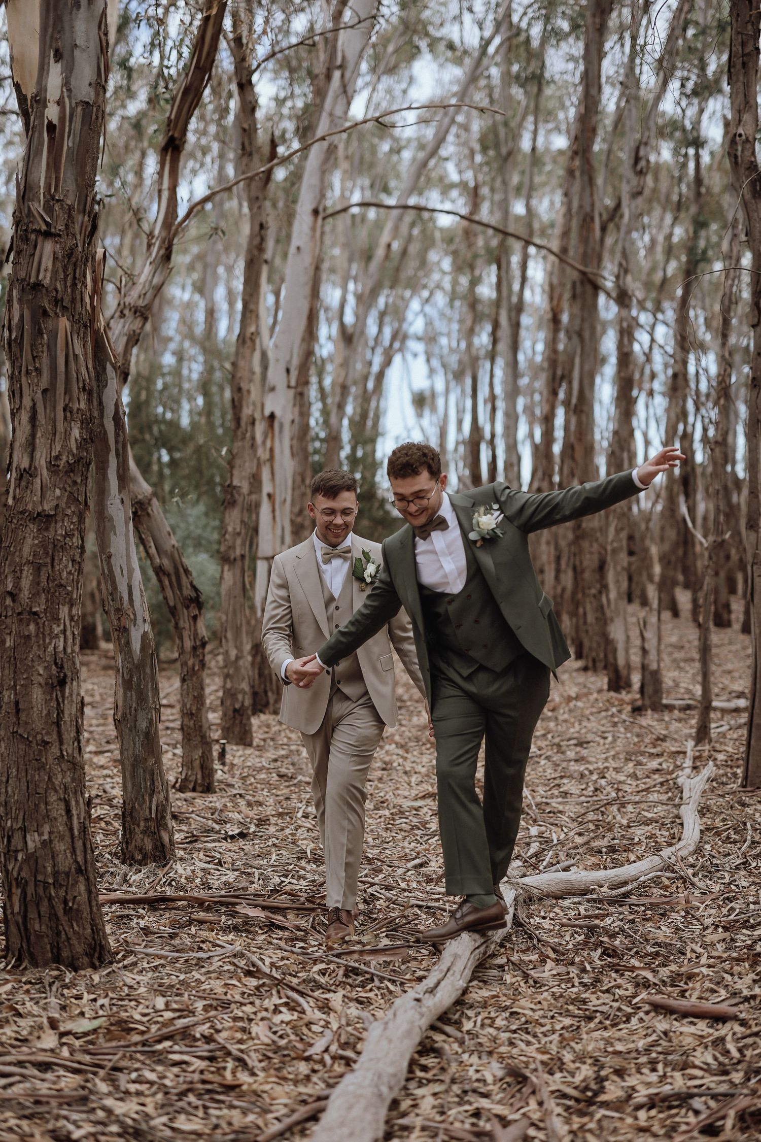 Two people in wedding attire playfully dancing and having fun in a wooded eucalyptus forest.