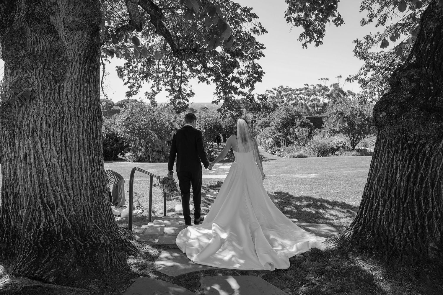 Black and white wedding photos arranged in a filmstrip style sequence showing outdoor ceremony moments under large trees.