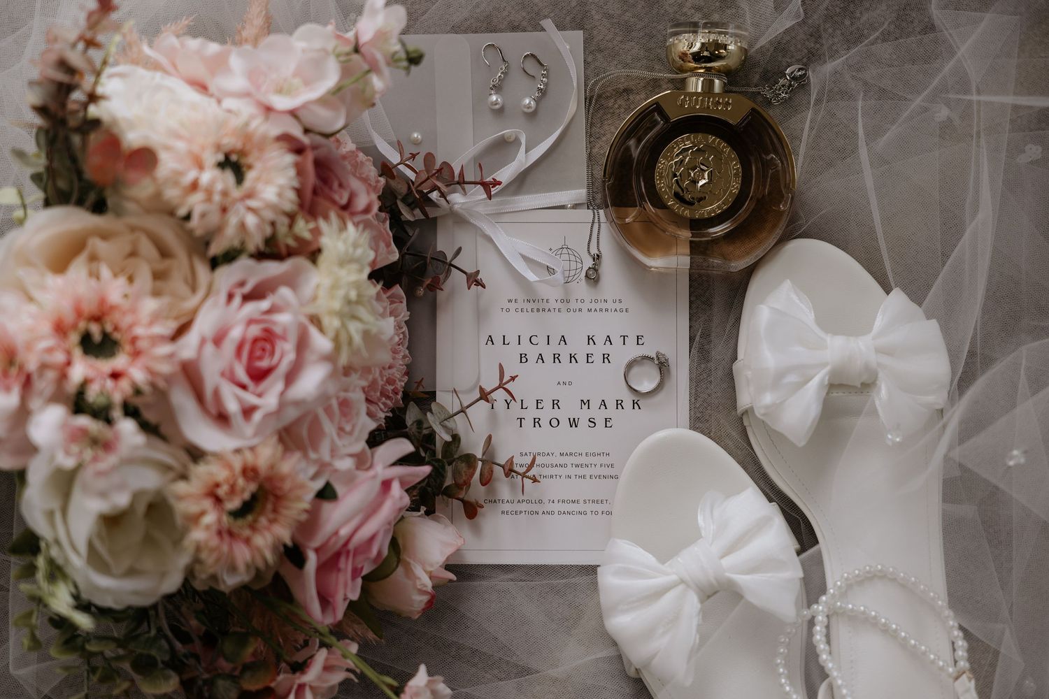 Wedding details including pink roses, invitations, and delicate accessories arranged on a light surface.