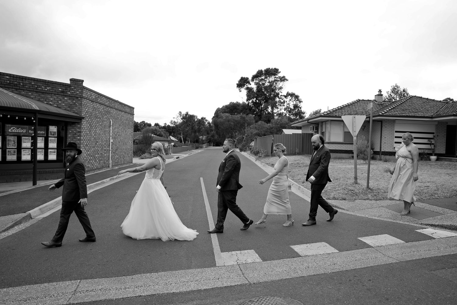 Multiple black and white frames capture a wedding party walking along a path in sequence.