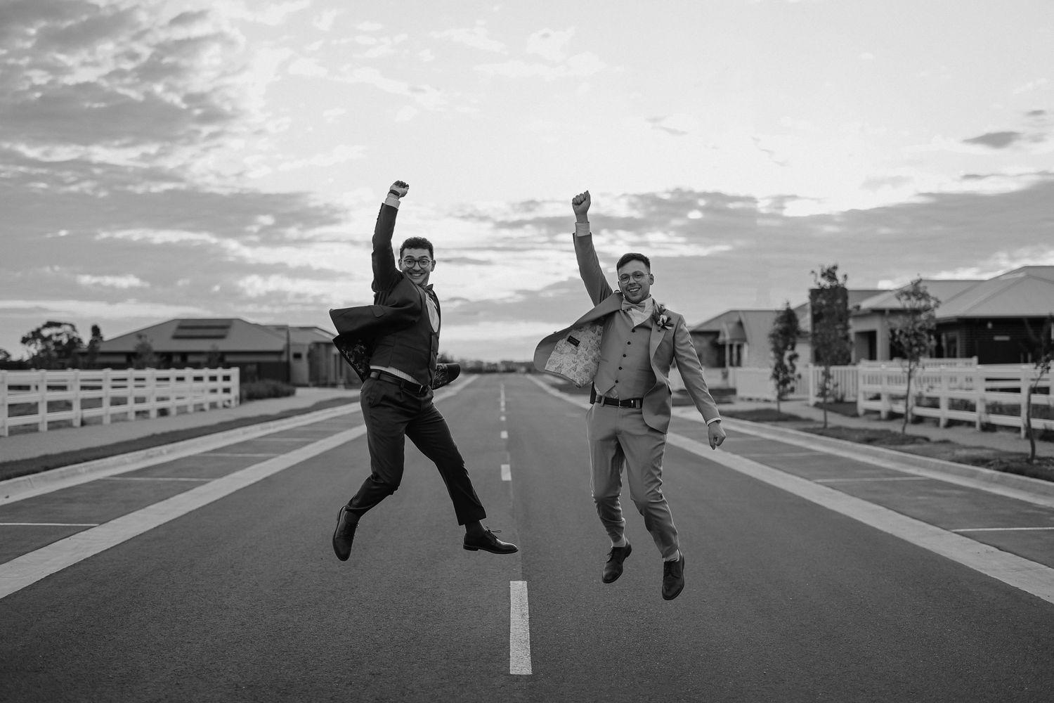 Two people jumping joyfully on an empty road at sunset with arms raised in celebration.