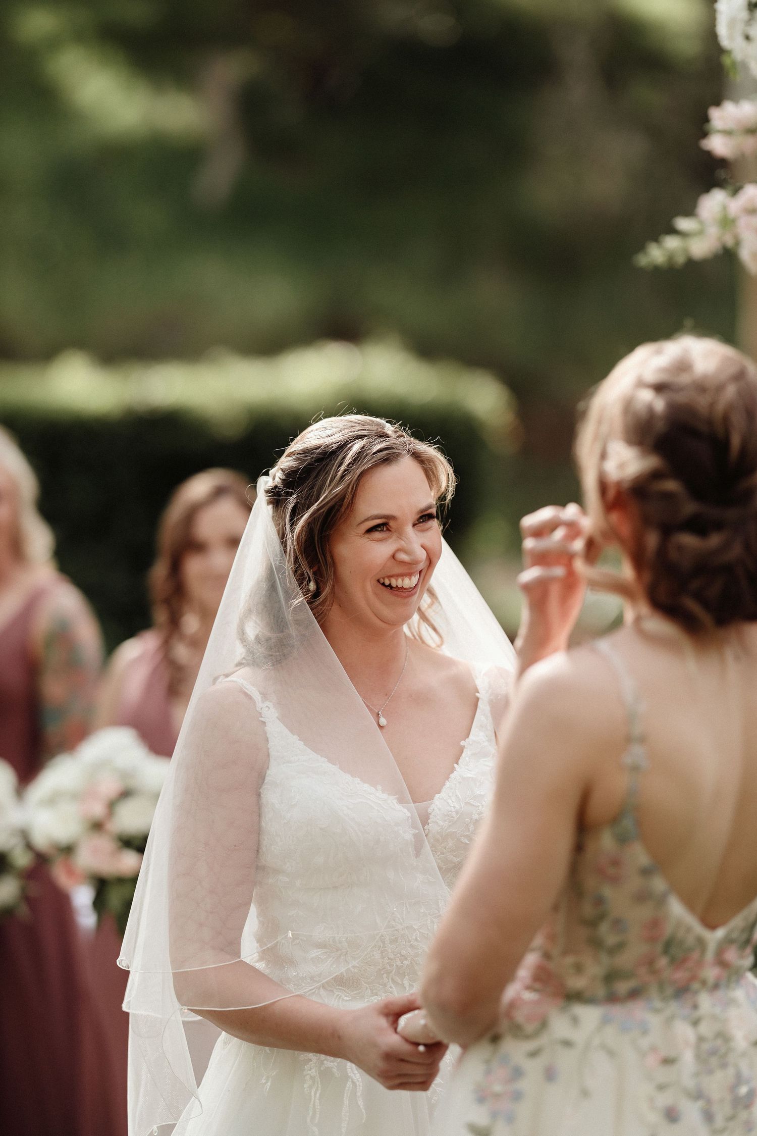 Wedding party members share joyful laughter during an outdoor celebration surrounded by greenery.