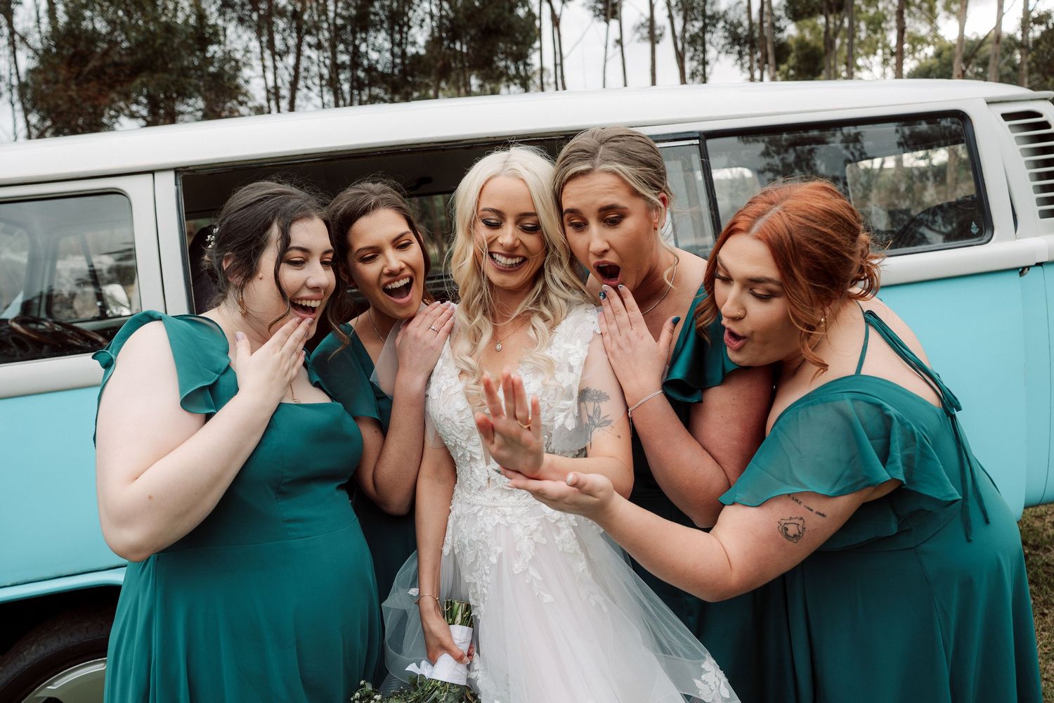 Wedding party gathered around vintage turquoise VW bus for photos.