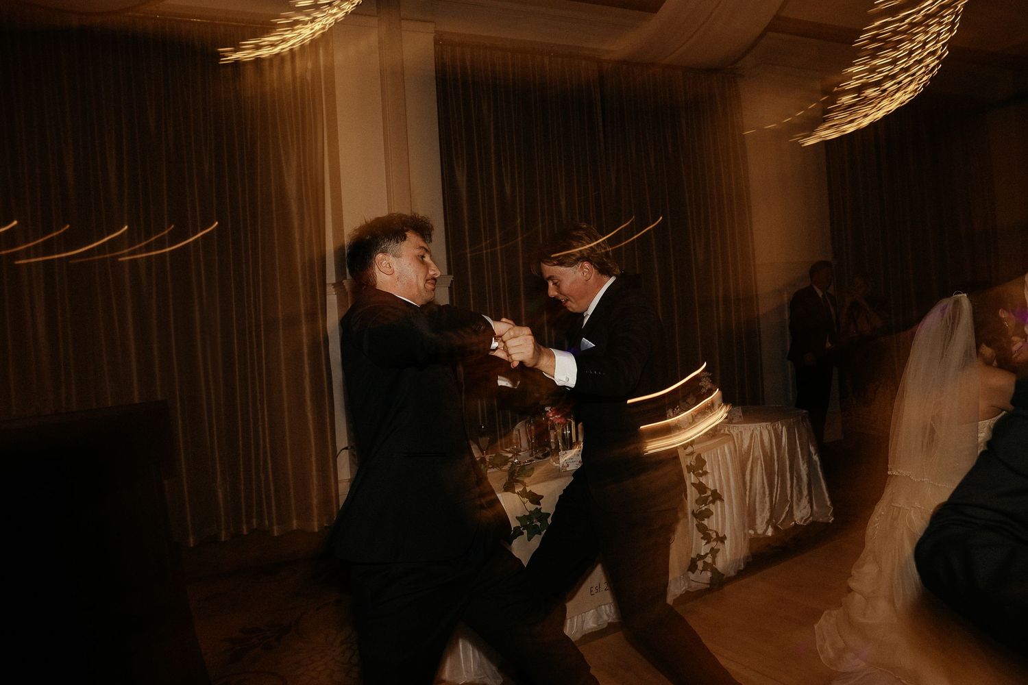 Wedding guests dancing and celebrating enthusiastically at an indoor reception.
