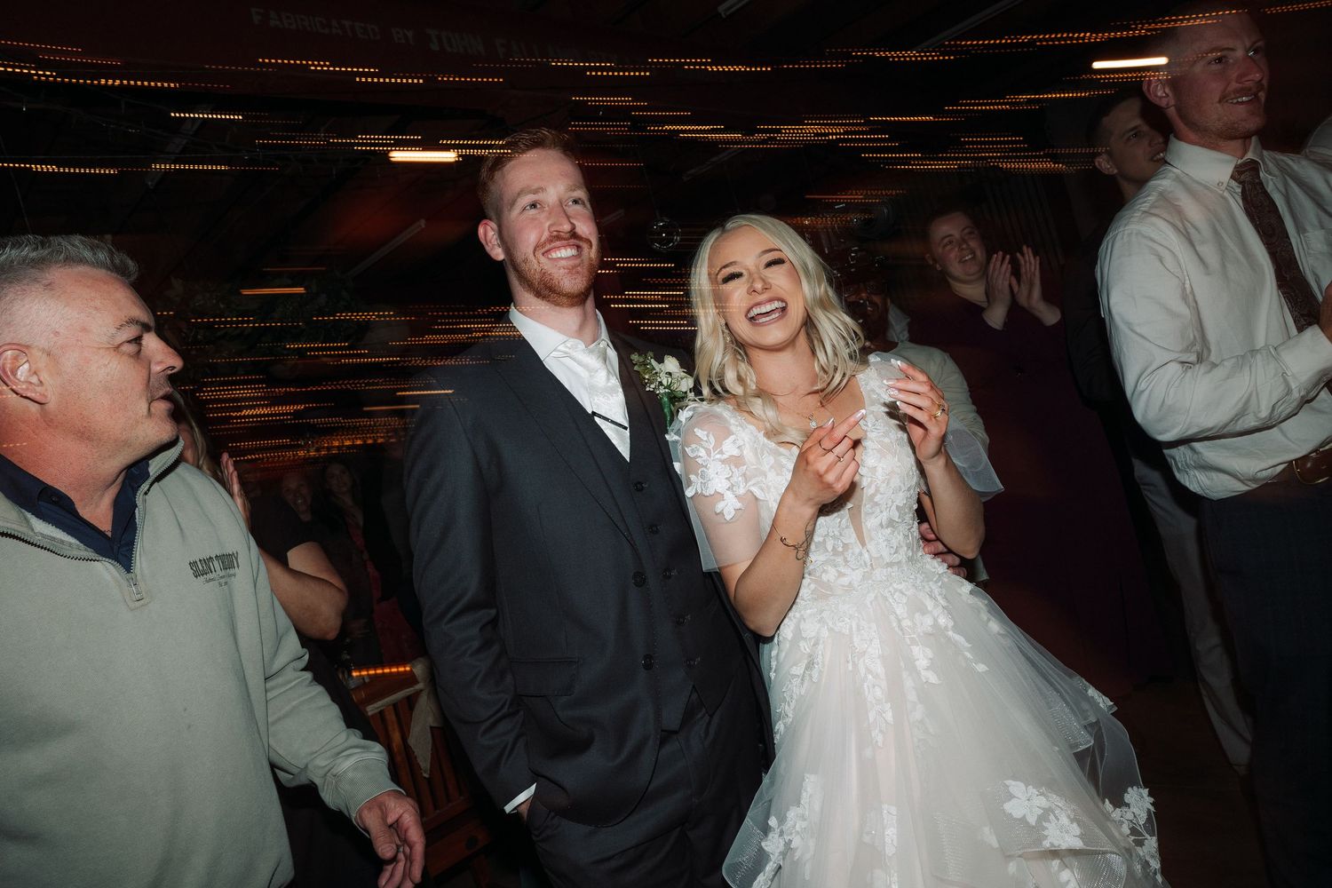 A couple shares a joyful moment on the dance floor at their wedding reception with guests nearby.