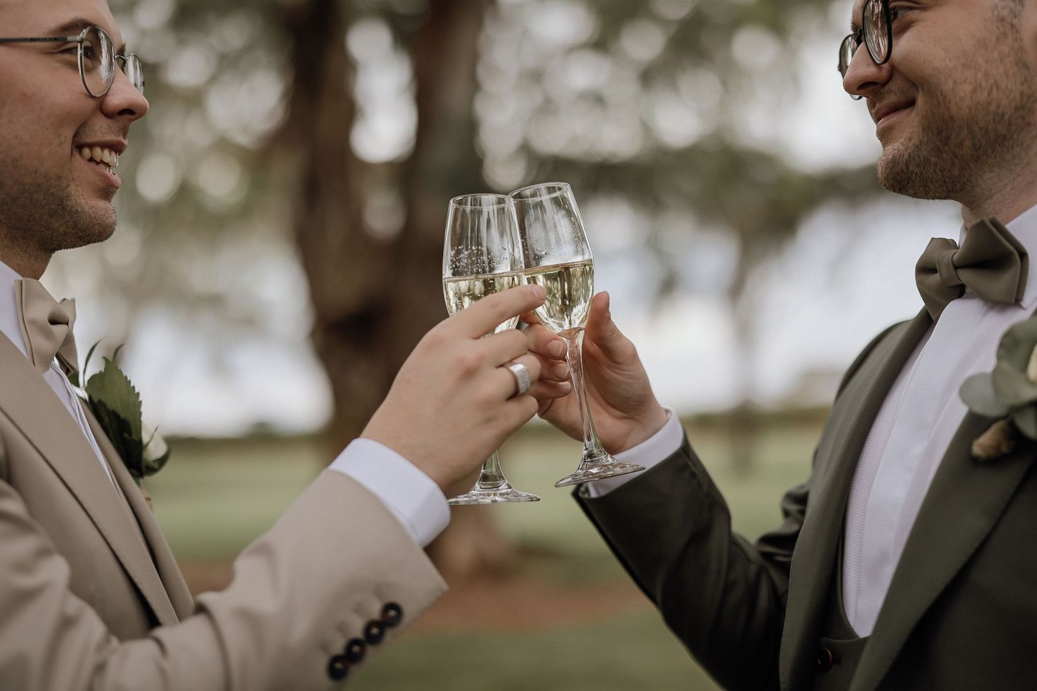 Two people in formal attire clink champagne glasses together during an outdoor celebration.