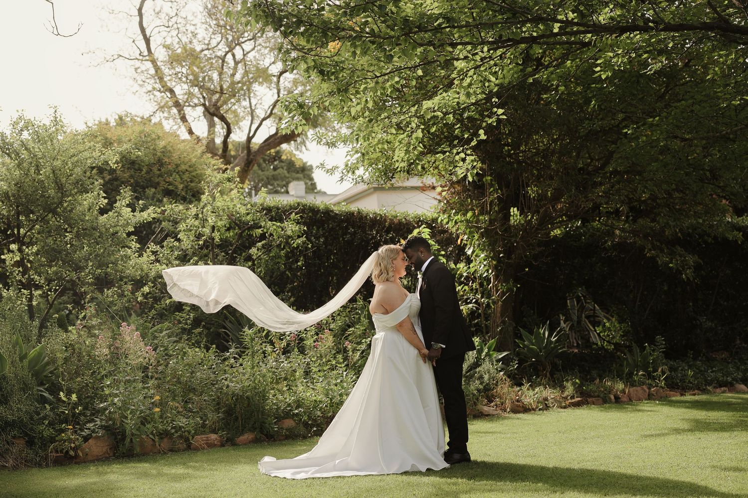 A wedding couple dances together in a lush green garden setting during their romantic outdoor celebration.
