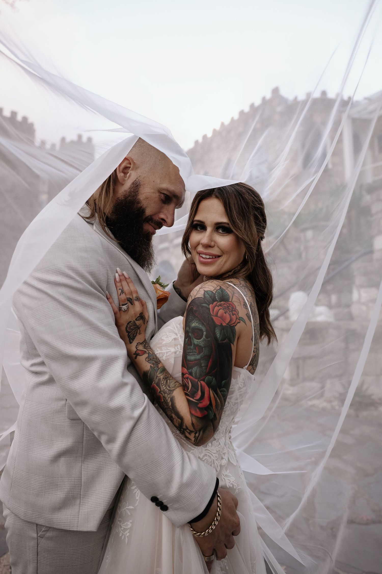A romantic wedding moment captured under a flowing veil with castle architecture in the background.
