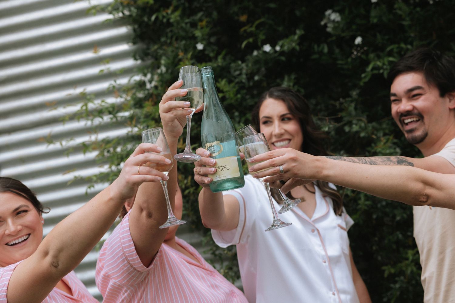 A group of friends laugh and raise their glasses in a celebratory toast outdoors.