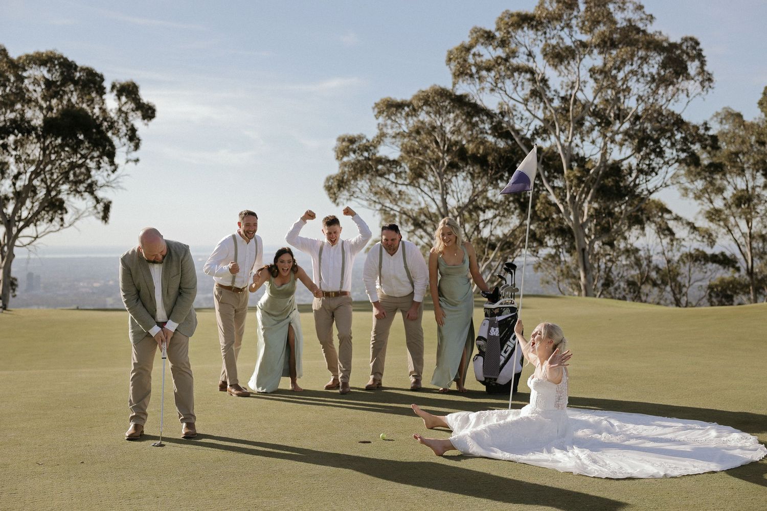 Wedding party poses playfully in a line on a grassy hilltop with eucalyptus trees in the background.