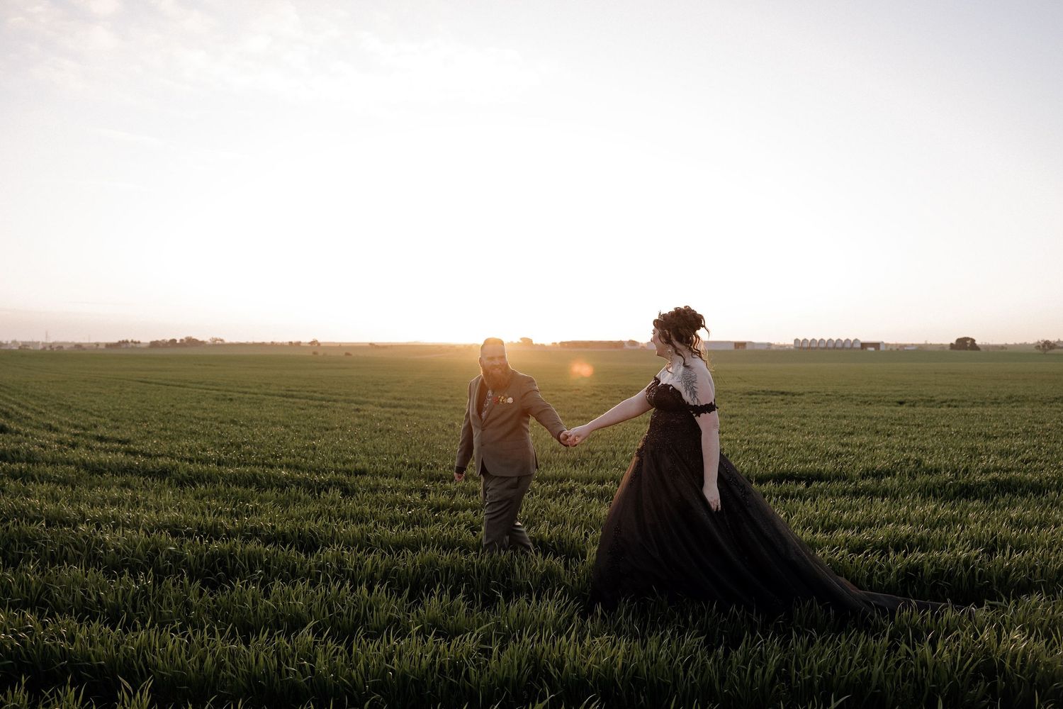 Silhouetted figures walk through a lush green agricultural field at sunset creating a dreamy countryside scene.
