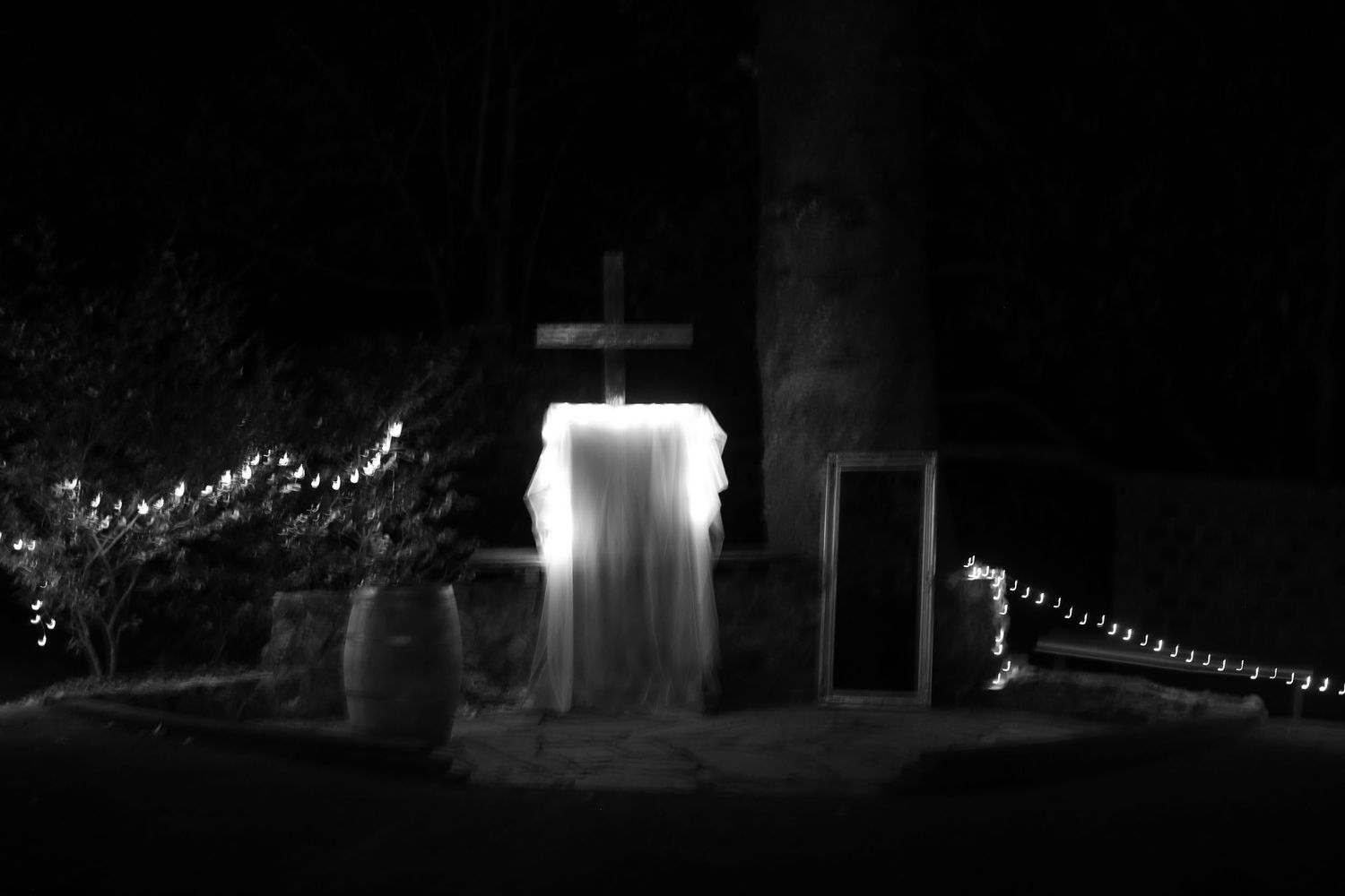 A glowing white ghostly figure illuminated at night stands between string lights in a spooky outdoor Halloween display.