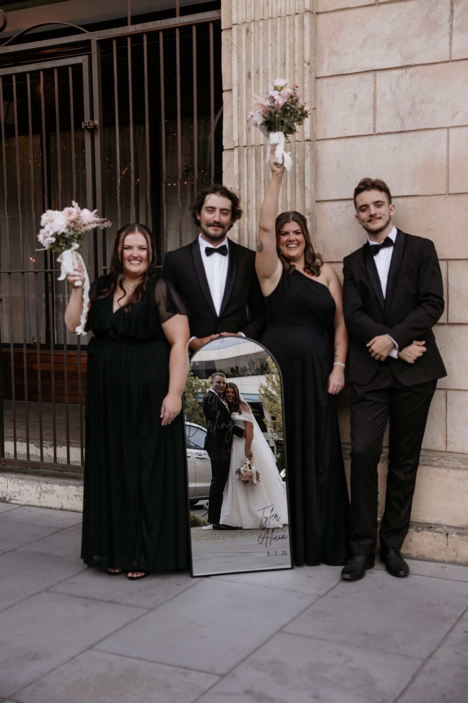 Wedding party in black formal attire poses progressively more casually in a series of four photos against stone wall.