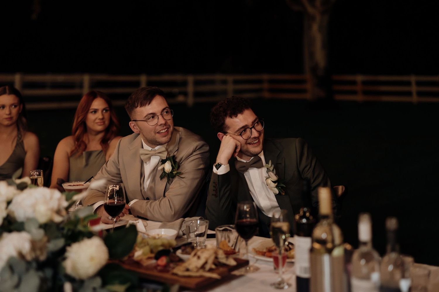 Wedding guests enjoy an outdoor reception dinner at long tables under string lights during an evening celebration.