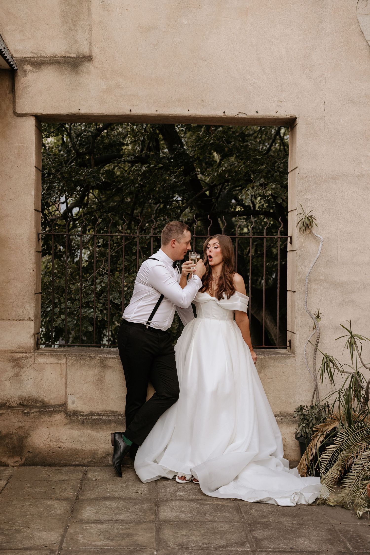 Romantic wedding couple poses against a textured wall in an outdoor setting.
