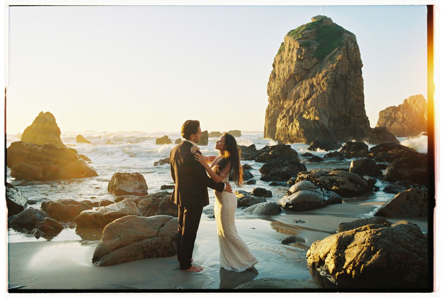Panoramic coastal scene with rocky cliffs and ocean waves at sunset.