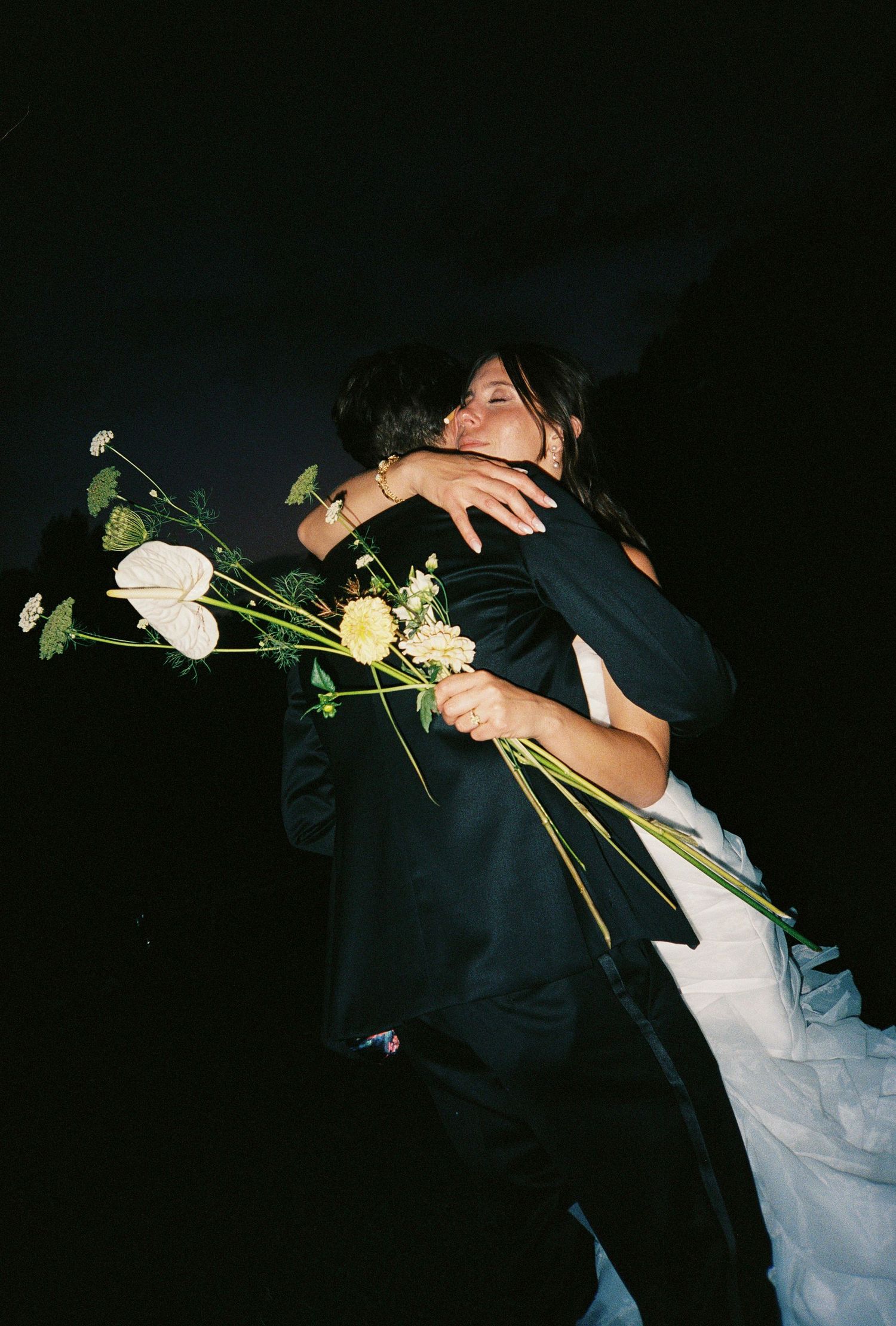 A couple in wedding attire embrace while holding white roses against a dark background in a series of romantic shots.